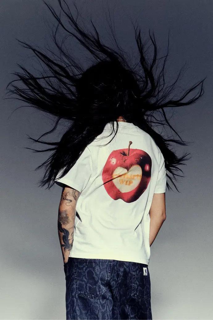 Personne de dos avec un tshirt blanc, ses cheveux noirs et longs volent au vent